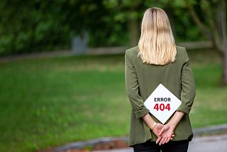 Frau steht rücklings in Natur und hält Schild mit Schriftzug "ERROR 404"