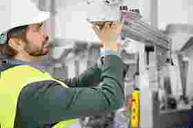 Man in high-visibility waistcoat and hard hat inspects machine part