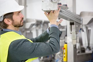 Man in high-visibility waistcoat and hard hat inspects machine part