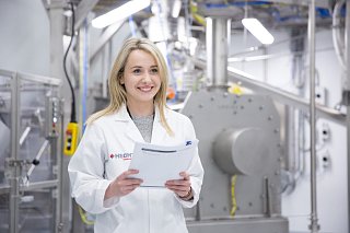 Woman smiling with a pad in her hand in front of a technical system