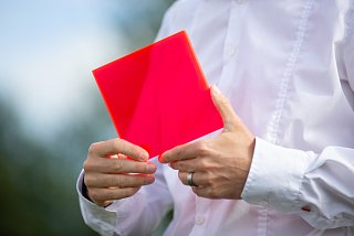 Person in weißem Hemd hält eine rote Raute in den Händen