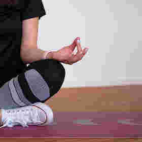 Person sitzt im Schneidersitz und meditiert auf einer Sportmatte