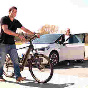 Mann mit schwarzem Fahrrad steht vor weißem Auto, in welches eine Frau einsteigt